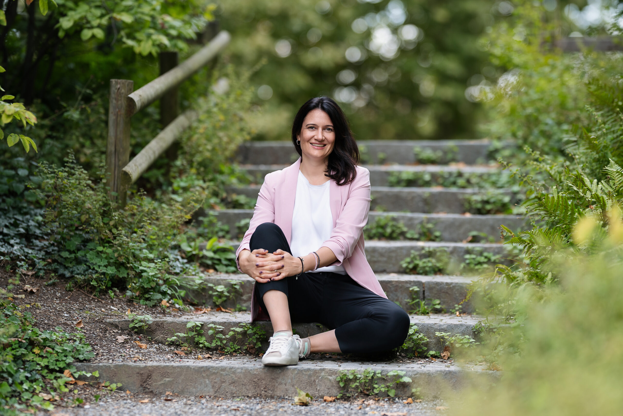 Präventiver Burnout Coach Cornelia Gürtler aus Zürich sitzt auf einer Treppe umgeben von grünen Bäumen und Sträuchern.